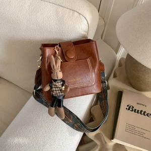 Detail of a brown wax leather bucket bag with ethnic style wide strap and rabbit charm
