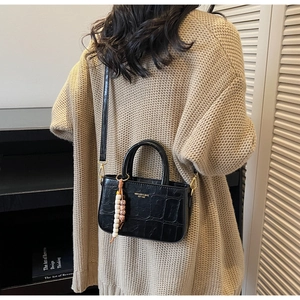 Detail of black crocodile embossed small square bag with wooden bead charm on model