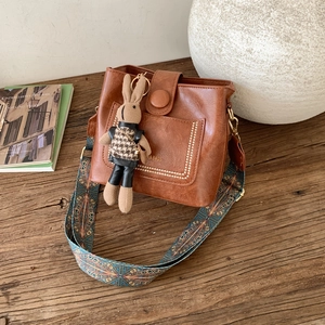 Detail of a brown leather crossbody bag featuring an ethnic wide strap and cute rabbit charm