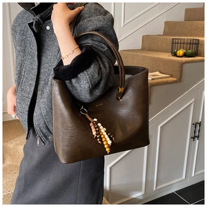 Détail du sac cabas en cuir marron foncé avec pendentif en perles et finition lisse