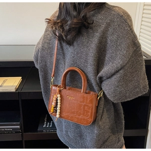 Brown crocodile embossed handbag with colorful bead charm worn by a model in a cozy sweater
