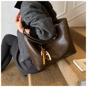 Détail du sac cabas en cuir marron foncé avec breloque en perles sur un mannequin