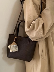 Minimalist dark brown leather bucket bag with plush charm and crossbody strap