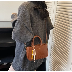 Detail of a brown crocodile pattern crossbody bag with a colorful beaded tassel charm