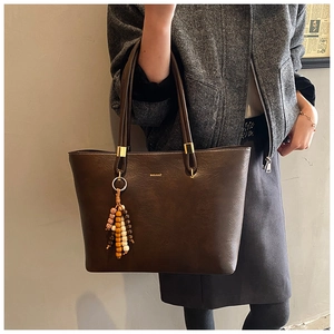 Détail du sac cabas en cuir marron foncé avec texture vintage et breloque perlée
