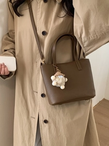 Brown leather bucket bag with adjustable strap and cute plush charm on trench coat