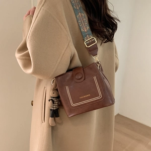 Detail of brown leather crossbody bag with ethnic style wide strap and rabbit charm
