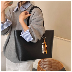 Détail d'un sac cabas en cuir noir grainé avec un pendentif à pampilles en perles