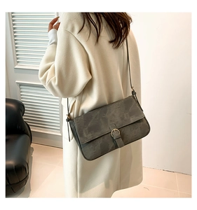Détail d'un sac à rabat vintage gris foncé avec boucle en bronze sur un manteau blanc