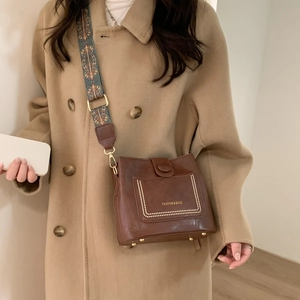 Close-up of brown crossbody bag featuring golden rivets and colorful woven wide strap