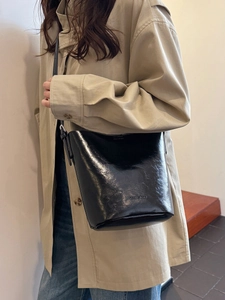 Glossy black patent leather bucket bag worn by model in a minimalist indoor setting