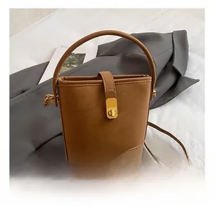 Detail view of tan bucket bag with gold metal buckle closure and adjustable strap