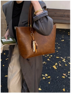 Détail d'un sac cabas marron en similicuir avec pompon en perles dans un décor d'automne