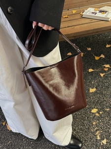 Vintage dark brown faux leather bucket bag with adjustable strap in an autumn outdoor setting