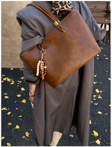 Détail du sac cabas vintage en cuir marron avec breloque ethnique et logo doré chic