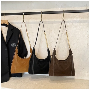 Detail of suede shoulder bags in brown and black with contrast stitching and chain straps