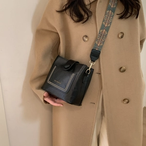 Detail of black leather crossbody bucket bag with ethnic wide strap on camel coat