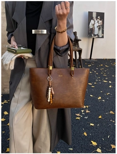 Détail du sac cabas marron vintage avec logo doré et pompon décoratif en perles
