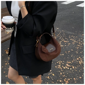 Detail of brown suede crescent bag with gold logo and crossbody leather strap