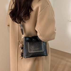 Detail of black textured crossbody bag with wide ethnic strap and bunny charm