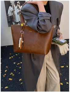 Gros plan sur un grand sac cabas en cuir marron foncé avec pompon en perles de bois
