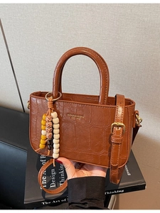 Brown crocodile pattern tote bag with wooden bead charm on black books