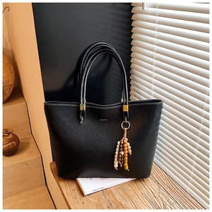 Détail d'un sac cabas en cuir texturé noir avec pompon en perles de bois et pièces dorées