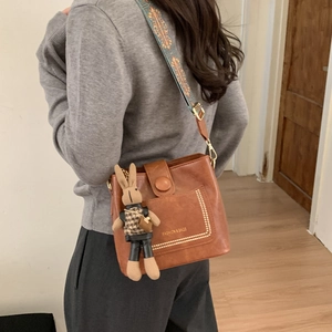 Detail of caramel brown bucket bag featuring ethnic embroidery strap and rabbit charm