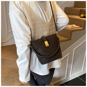 Detail of dark brown bucket bag with gold lock buckle and minimalist crossbody strap