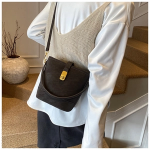 Close-up of minimalist dark brown bucket bag with gold metal clasp on a female model