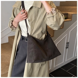 Detail of dark brown faux suede tote bag with adjustable strap worn with a trench coat