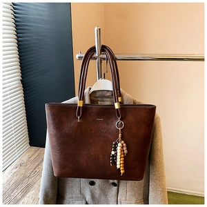 Gros plan sur le sac cabas en similicuir marron avec logo doré et pompon en perles