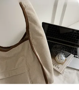 Detail of corduroy shoulder bag with brown trim next to laptop and headphones
