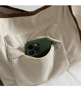 Detail view of corduroy tote bag front zipper pocket holding a green smartphone