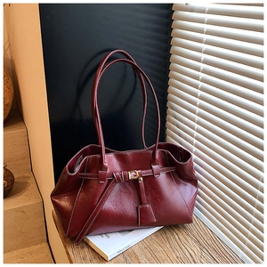 Detail of burgundy leather tote bag with knot strap and metallic buckle on wooden surface