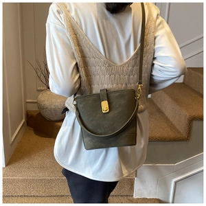 Close-up of olive green bucket bag with gold buckle on model in warm lighting