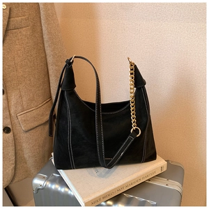 Detail of black hobo bag showing contrast stitching, long strap, and gold chain accent