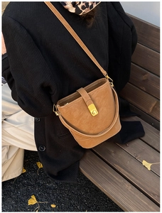 Brown bucket bag styled with a black coat on a bench, showcasing fall fashion look