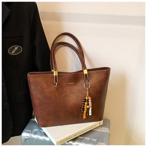 Détail du sac cabas en cuir marron foncé avec charme en perles de bois sur une valise