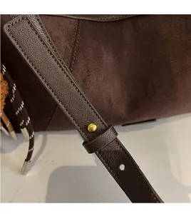Détail d'un sac en daim marron foncé avec bandoulière en cuir et rivets dorés