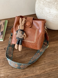 Vintage brown leather crossbody bag with ethnic strap and rabbit charm on a desk