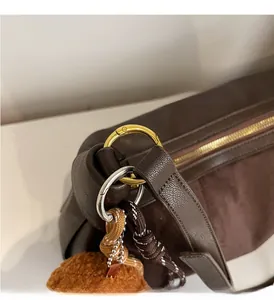 Détail du sac à bandoulière en cuir grainé avec anneaux dorés et pompon décoratif
