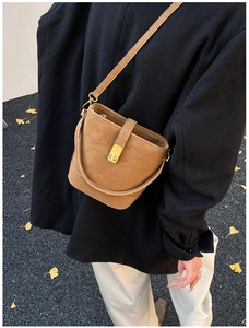Close-up of brown bucket bag with gold clasp shown on model against autumn leaves