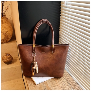 Détail du sac cabas en cuir marron foncé avec logo doré et pompon en perles de bois