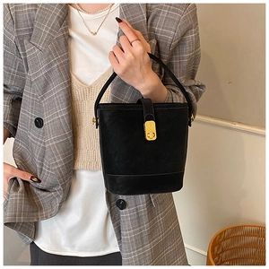 Detail of black matte leather bucket bag featuring a rectangular gold metal twist lock