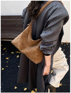 Close-up of brown suede hobo bag with stitching detail on model in autumn park setting