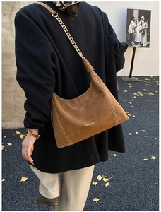Detail of brown suede hobo bag with contrast stitching and gold chain on a model