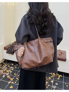 Detail view of brown suede tote bag featuring adjustable side straps and plush bear charm