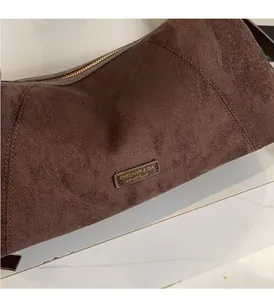 Gros plan sur la texture en daim marron foncé et le zip doré du sac sous le bras