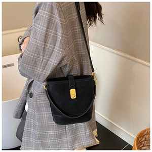 Detail of a black leather bucket bag with gold circular lock worn by a model